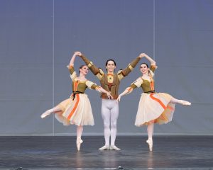 A male dancer poses on stage with one female dancer on either side of him.
