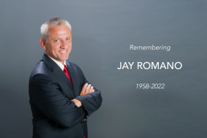 A headshot of Jay Romano to the left smiling with his arms crossed.